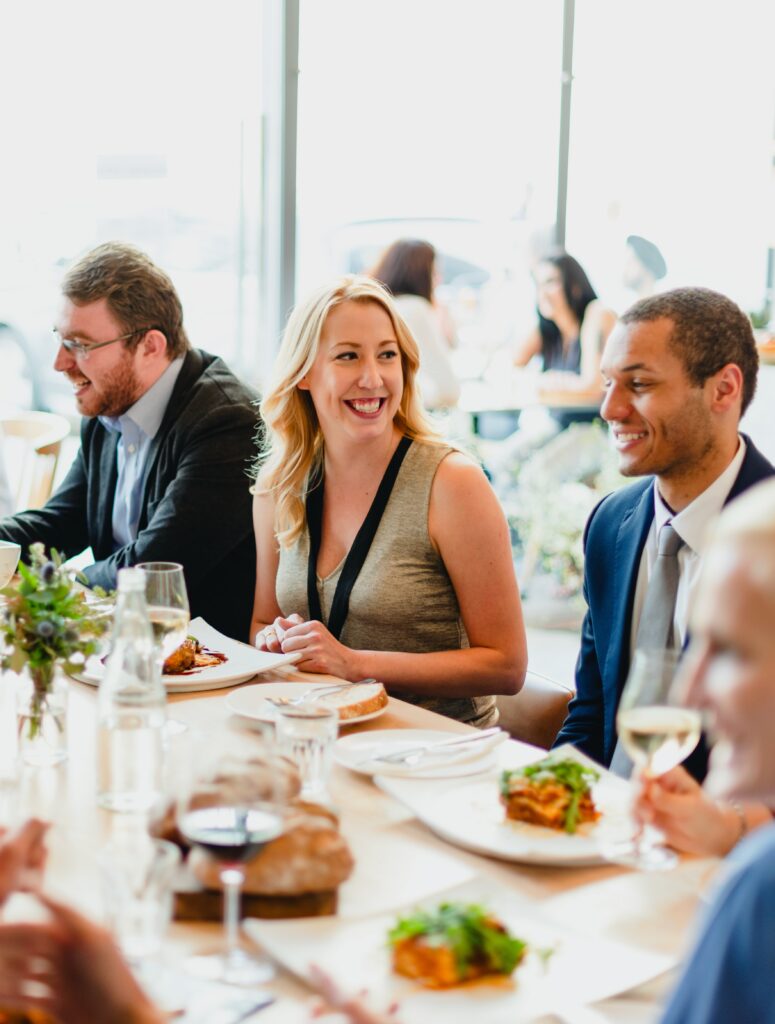 a diverse group of people enjoying a lively dinner party. the scene features men and women of various ethnicities, sharing laughter and delicious food at a beautifully set table.